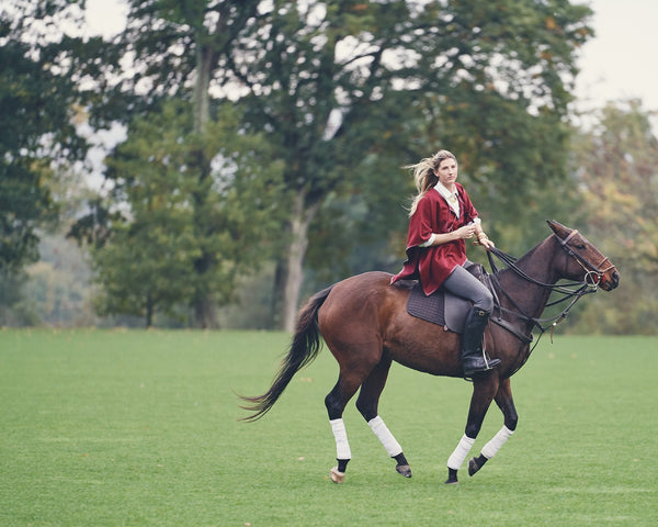 Woman riding a horse wearing an Alpaca Leather Trim Tassel Poncho in Burgundy - Stick & Ball