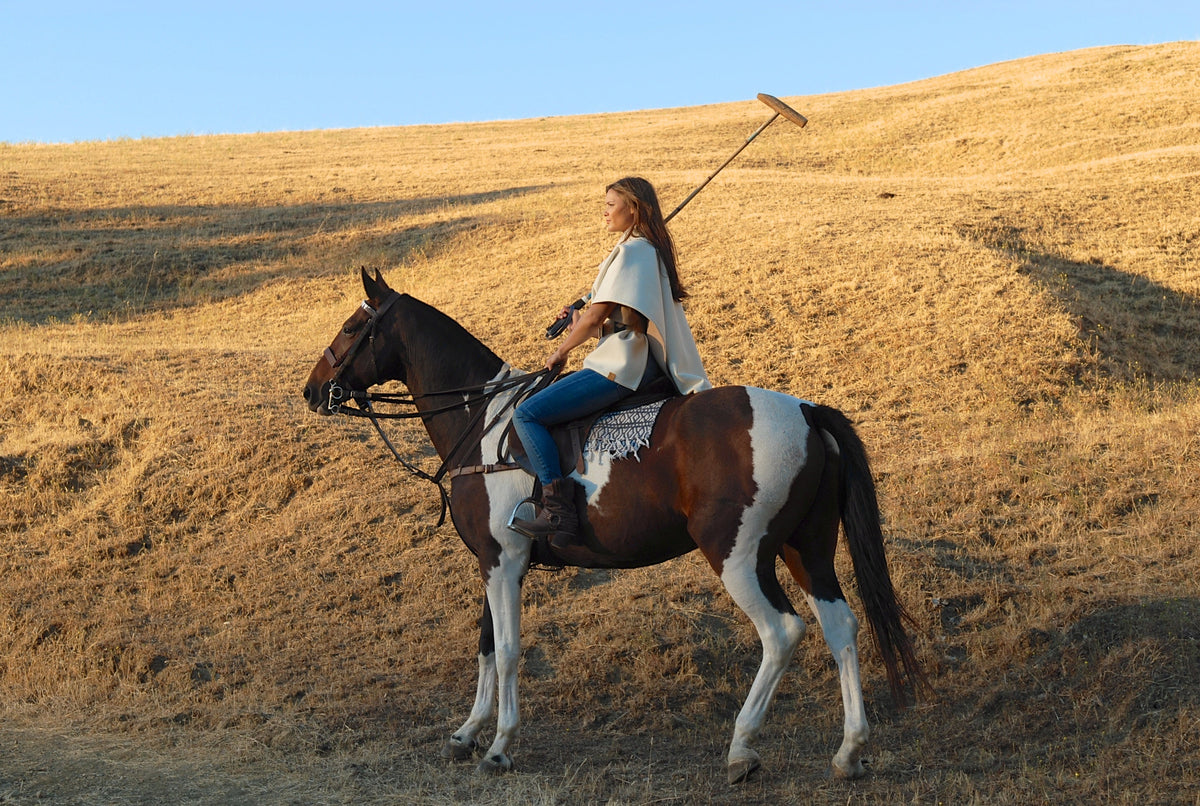 Model on polo horse wearing white Stick and Ball poncho
