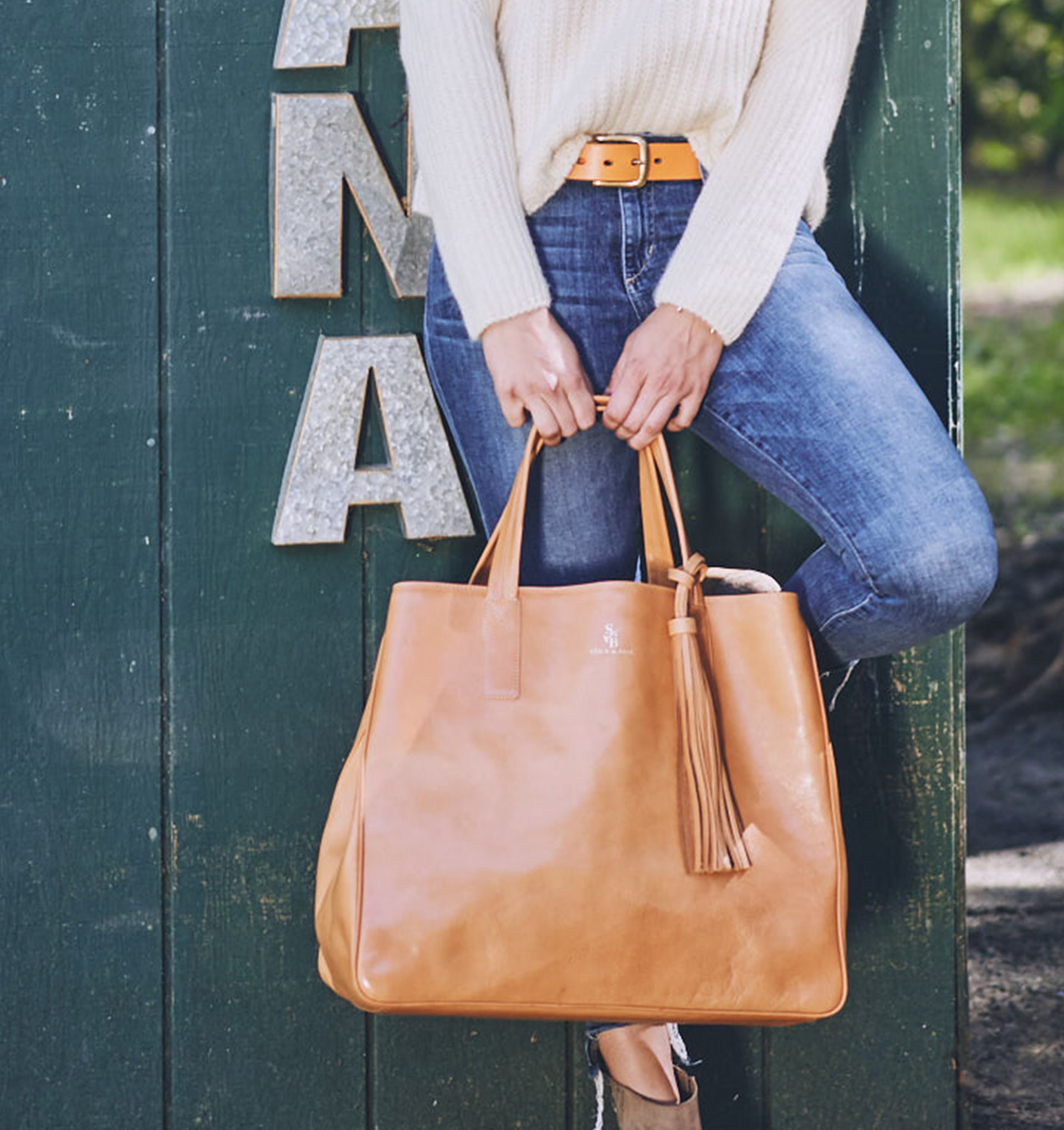 woman-wearing-stick-and-ball-accessories-leather-belt-inca-polo-belt-orange-and-holding-the-wellington-weekender-bag-in-tan