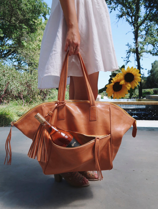 Woman holding the Palermo Soho Tote Bag in tan with a bottle of rose from Sinnegal Estate Winery 