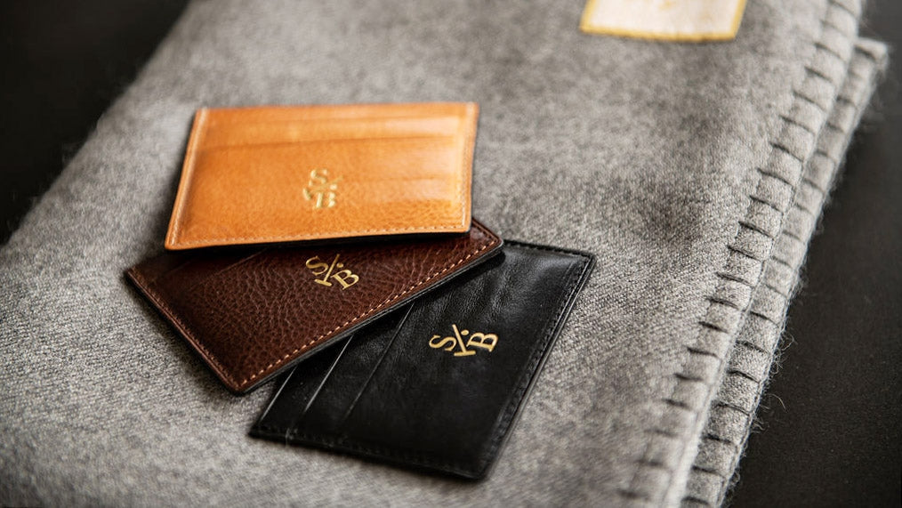 Collection image for Men's Leather & Woven Wallets - Assortment of tan, brown, and blacl flat leather wallets on Grey alpaca throw